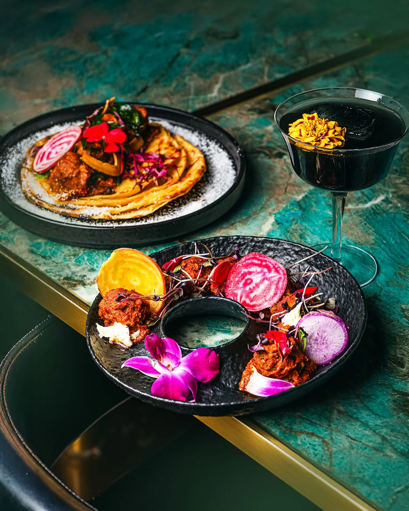 Indian dishes and a floral cocktail on a green marble table